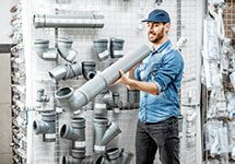 A man holding a pipe in front of pipes.