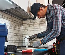 A man in plaid shirt and gloves working on sink.