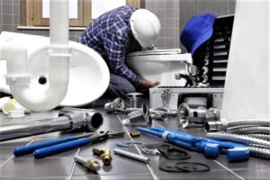 A man working on a toilet with many tools around him.