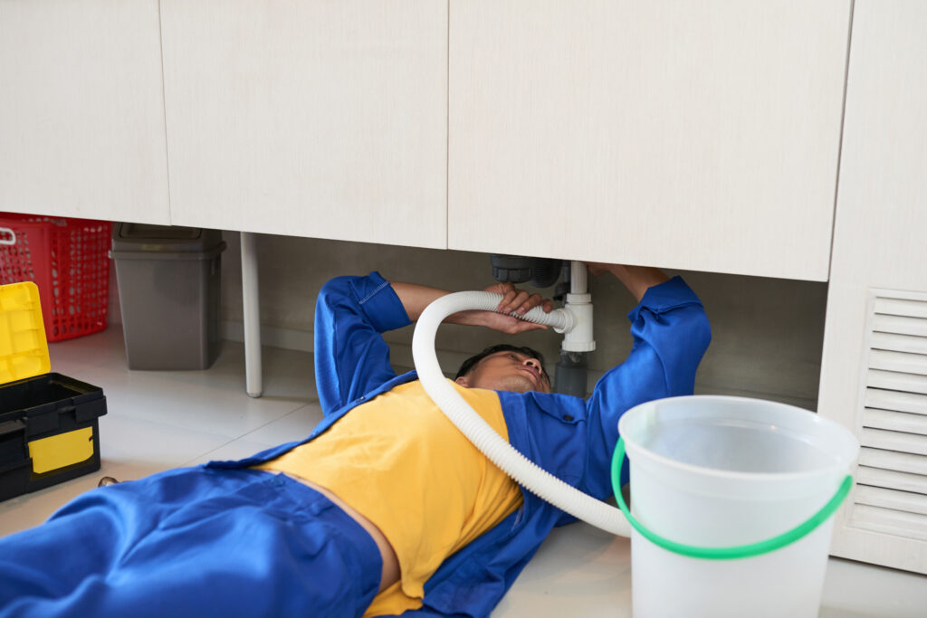 A person laying under the sink with an hose attached to it.