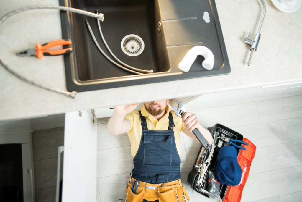 A man in an apron is fixing the sink.